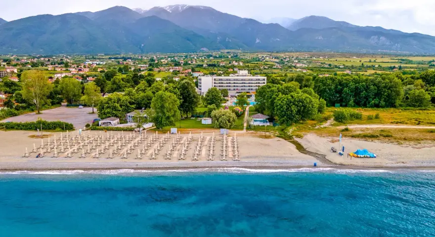 Piękna plaża na Riwierze Olimpijskiej z rzędami leżaków, hotelem i górami w tle.