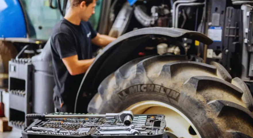 Mechanik sprawdza poziom płynów eksploatacyjnych w traktorze, obok leży zestaw kluczy.