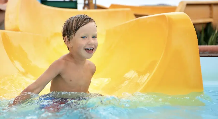 Ein Junge mit blauen Augen lacht fröhlich im Wasser der Wasserrutsche im Heidebad Torgelow.