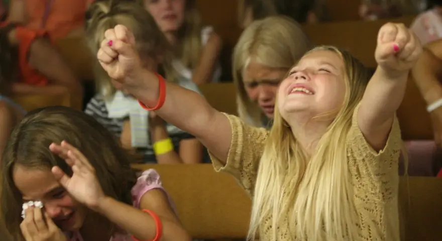 Junge Mädchen erleben emotionale Momente bei einer evangelistischen Religionsveranstaltung, eine jubelt, die andere weint.