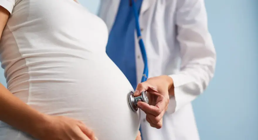 Lekarz osłuchuje brzuch ciężarnej kobiety stetoskopem. Dbałość o zdrowie w ciąży to podstawa.