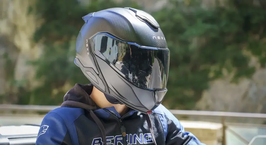 Casco da moto nero con visiera riflettente, che offre una sensazione di pressione sulla fronte. Indossato da una persona con giacca blu e nera.