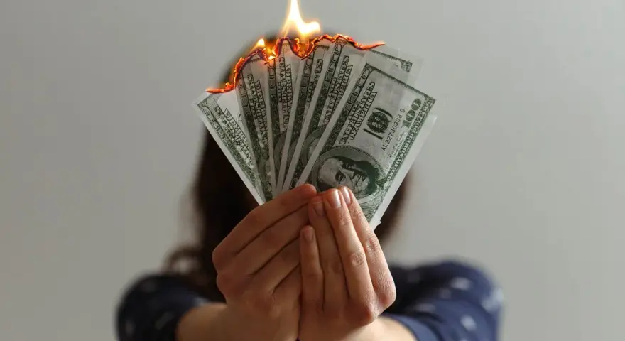 Hands hold burning US dollar bills, a visual metaphor for a use it or lose it budget.