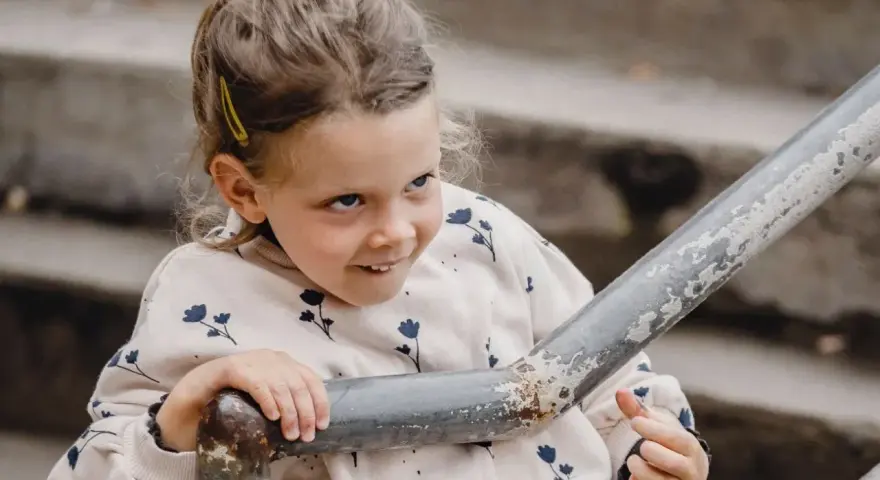 Mała dziewczynka z spiętymi włosami i spinką, w bluzie w kwiatki, opiera się o poręcz. Jej spojrzenie sugeruje dziwne zachowanie 2,5 latka.