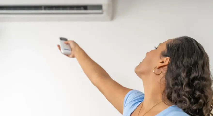Donna con telecomando regola il condizionatore, la canalina condizionatore design si integra perfettamente.