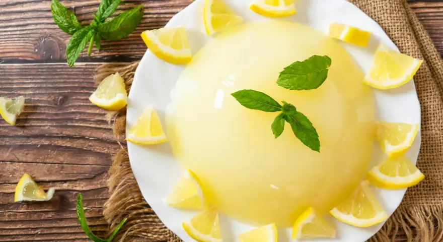 Delizioso gelo di limone su piatto bianco, decorato con spicchi di limone fresco e foglie di menta.