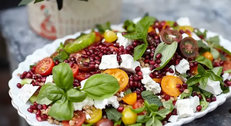 En färgglad sallad med granatäpple, tomater, fetaost och basilika, perfekt som sallad till grillat.