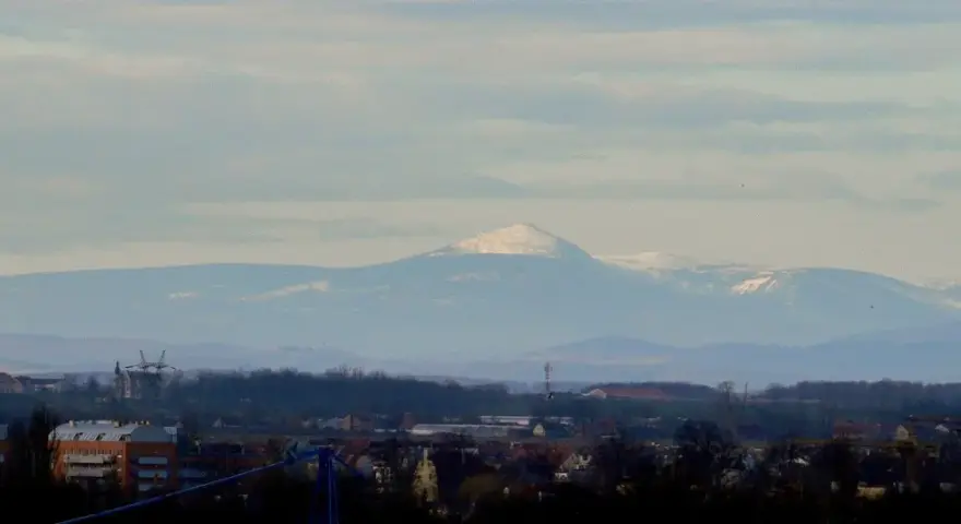 Widok na Śnieżkę i Karkonosze z Wrocławia. Widać ośnieżone szczyty górskie na tle błękitnego nieba.