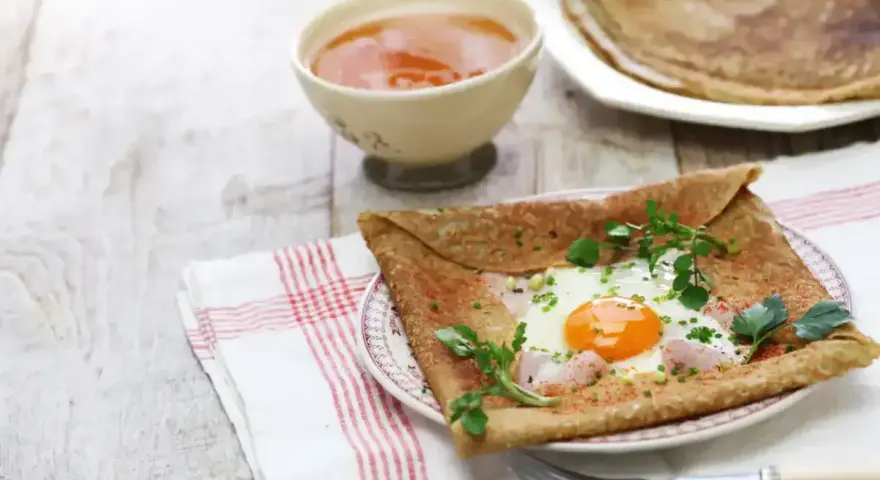 Crêpe de sarrasin garnie d'un œuf au plat, de jambon et d'herbes fraîches, servie avec une compote.