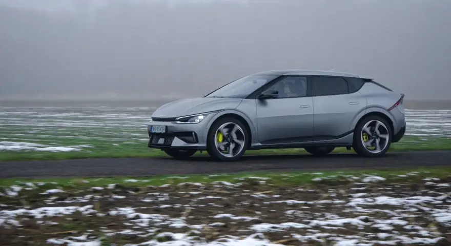 Srebrna Kia EV6 jedzie po drodze, otoczona polami z resztkami śniegu.