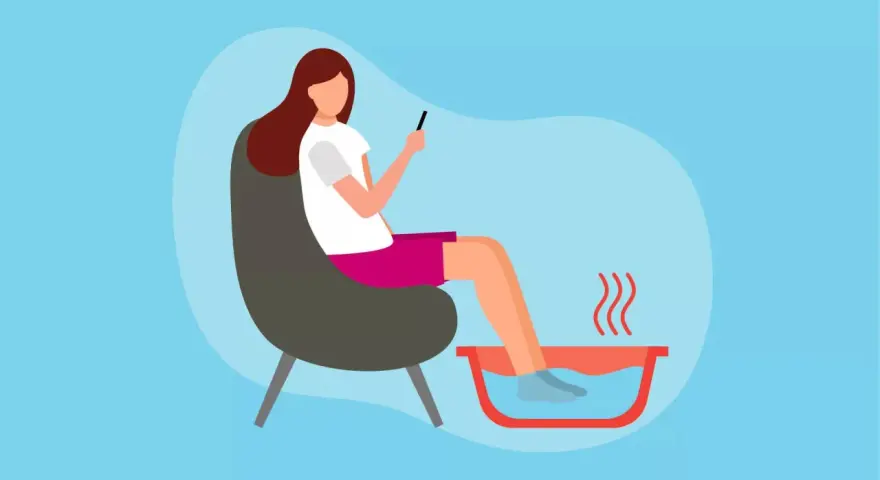 A woman relaxes in a chair, enjoying a soothing foot soak while scrolling on her phone.
