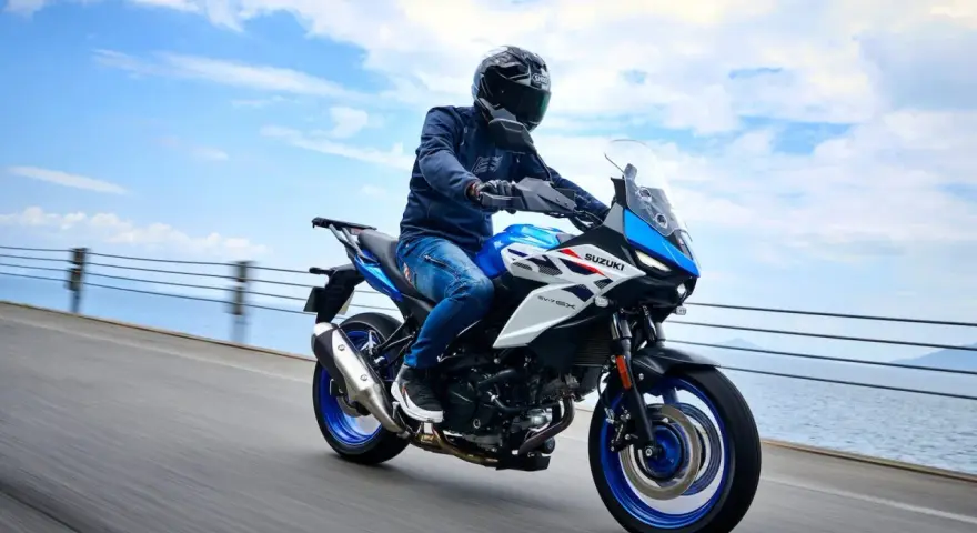 Motocyklista na niebiesko-białym Suzuki SV650X, idealnym motocyklu do 35kW, jedzie wzdłuż wybrzeża.