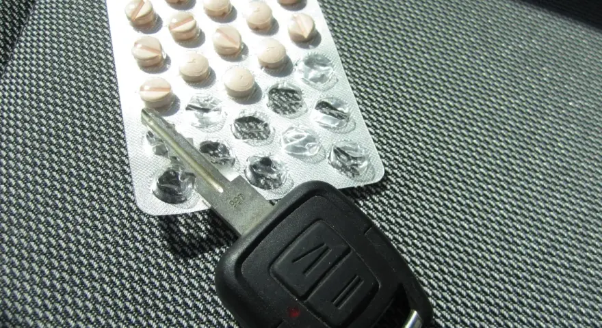Tabletten und Autoschlüssel liegen nebeneinander. Tilidin autofahren ist gefährlich und illegal.
