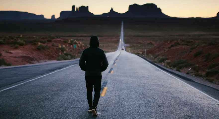 Człowiek idzie pustą drogą w Monument Valley, pogrążony w mysleniu tunelowym, z widokiem na skalne formacje w oddali.