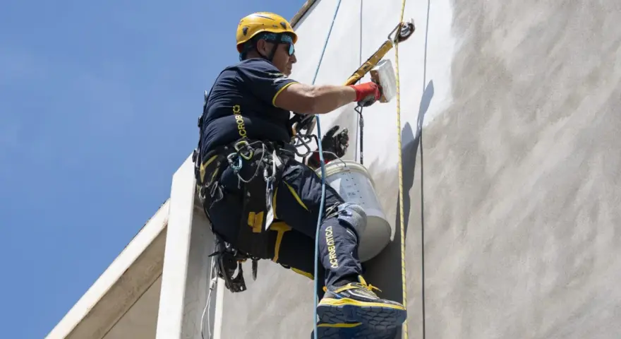 Trabajador en altura realiza instalación SATE, aplicando revestimiento en fachada con equipo de seguridad.