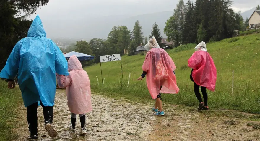 Deszcz w Zakopanem? Nic nie szkodzi! Rodzina w kolorowych pelerynach idzie ścieżką do kasy biletowej, ciesząc się widokami.