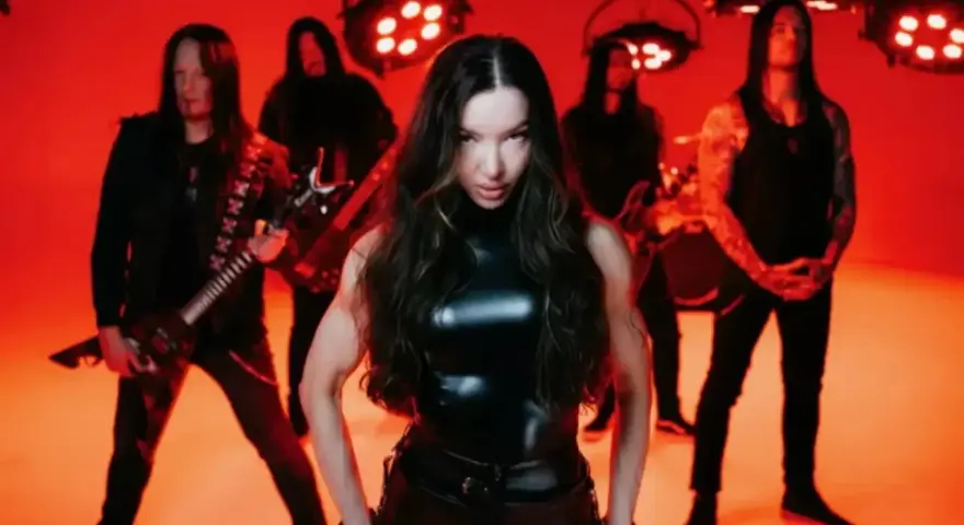 Wokalistka zespołu Arch Enemy w czarnym, błyszczącym stroju, z gitarzystami w tle, na tle czerwonych świateł.