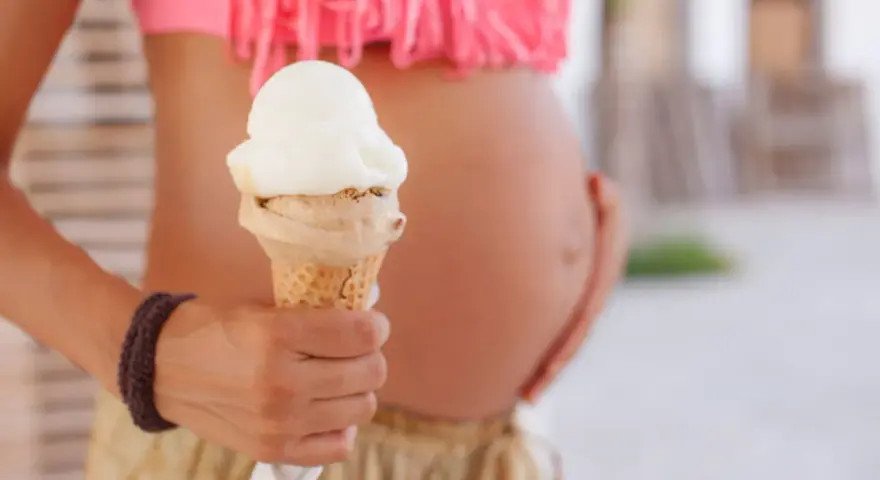 Schwanger und Lust auf Eis? Eine Frau hält ein Eis in der Hand, während sie ihren Bauch streichelt.