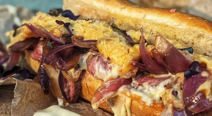 Ein saftiger Philly Cheesesteak-Sandwich mit geschmolzenem Käse, karamellisierten roten Zwiebeln und zartem Rindfleisch auf einem Baguette.