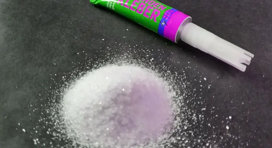 A pile of white granular material sits next to a tube of "Sekunden Kleber" super glue, ready for a quick fix.
