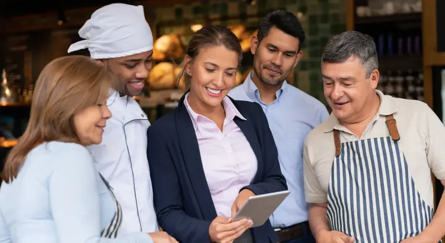 Equipo revisando tablet para la gestión de restaurantes. Chef, gerentes y personal colaboran.