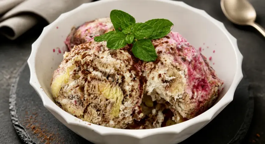 Schüssel mit Zuppa Inglese Gelato, garniert mit Minze und Schokoladenraspeln. Ein Löffel liegt daneben.