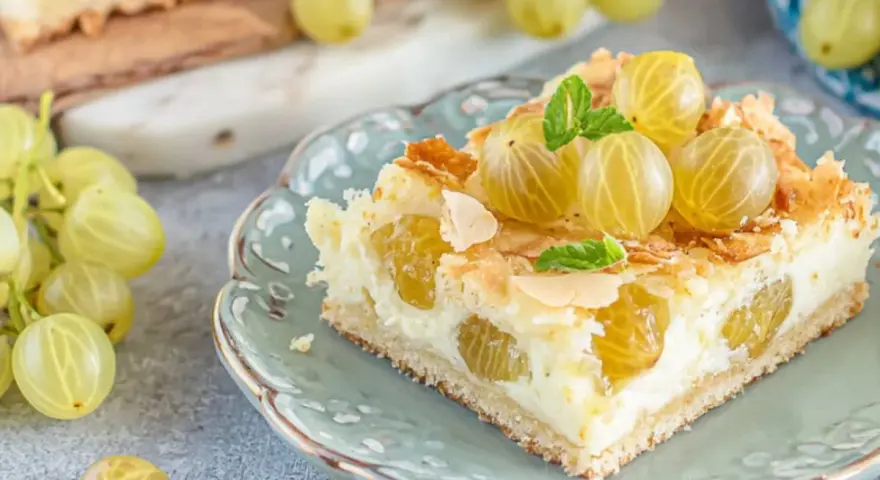 Ein Stück von die besten stachelbeerkuchen, garniert mit frischen Stachelbeeren und Mandelsplittern, auf einem zartblauen Teller.