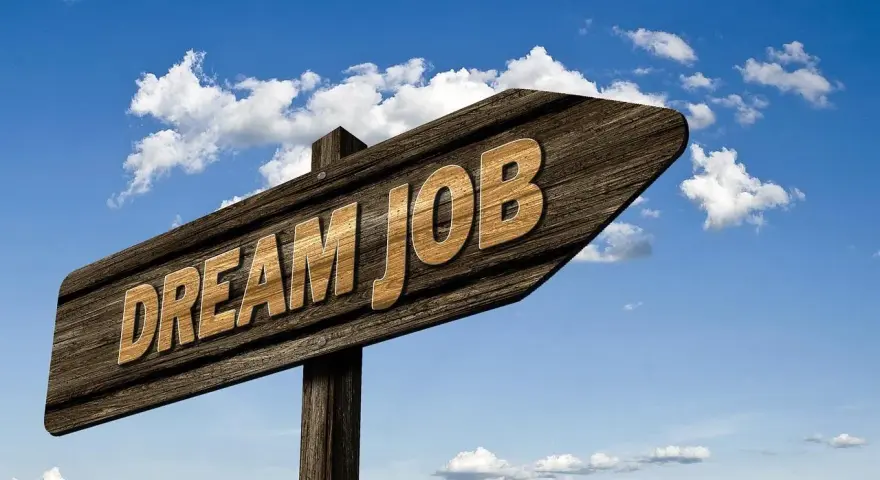 Drewniany drogowskaz z napisem "DREAM JOB" na tle błękitnego nieba z chmurami.
