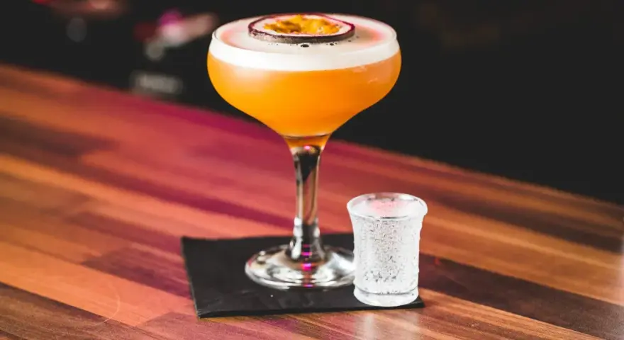 Orzeźwiający passion fruit martini z pianką i plasterkiem owocu, obok kieliszek wody gazowanej. Idealny na letnie wieczory.