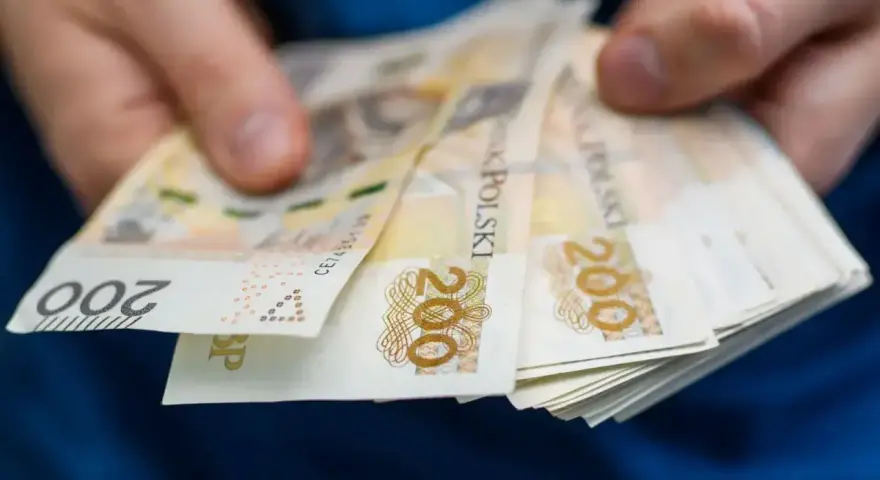 Dłonie trzymają stos banknotów 200 zł. Pieniądze mogą posłużyć do zapłaty czynszu administracyjnego.