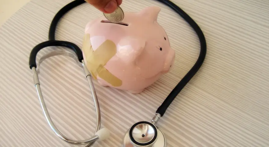 Salvadanaio a forma di maialino con cerotti, uno stetoscopio e una mano che inserisce una moneta. Simboleggia il dottore stipendio e la cura delle finanze.