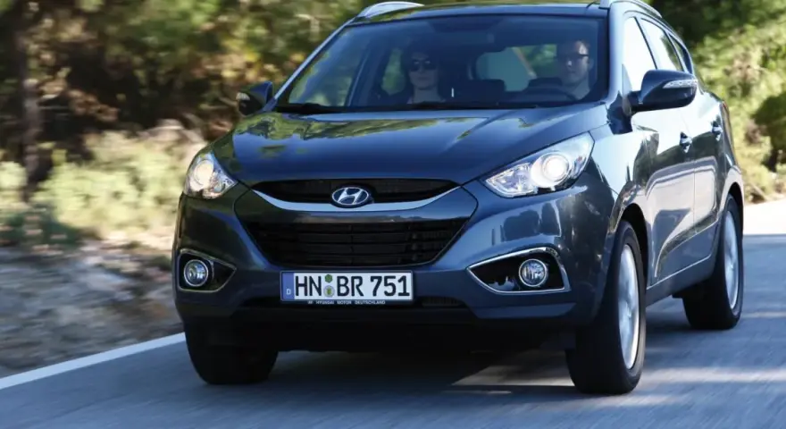 Dunkelgrauer Hyundai ix35 fährt auf einer Straße. Fahrer und Beifahrerin sind zu sehen. Mögliche Hyundai ix35 Probleme sind hier nicht ersichtlich.