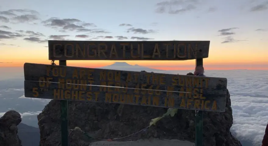 Gratulacje! Jesteś na szczycie Mount Meru, 5. najwyższej góry Afryki. Widok na morze chmur i wschód słońca zapiera dech w piersiach.
