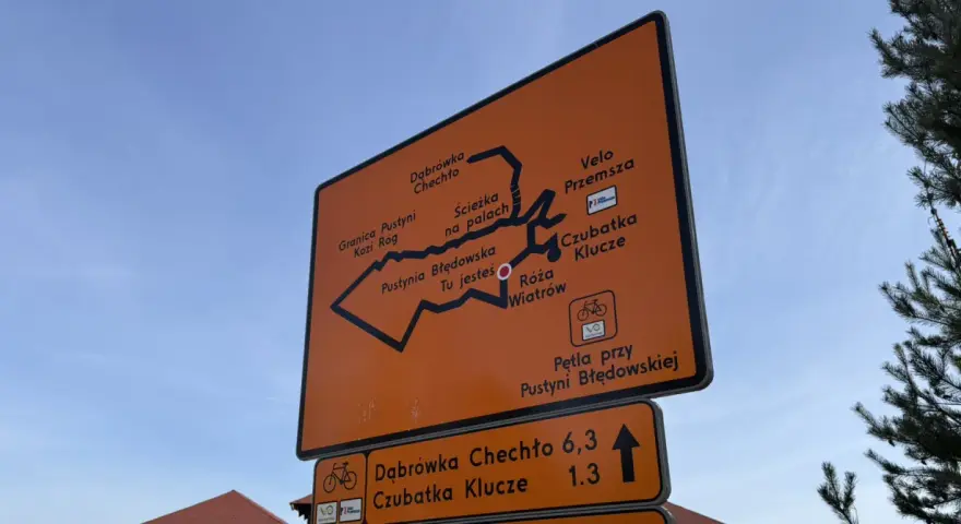 Pomarańczowa tablica z mapą szlaków rowerowych Velo Przemsza. Wskazuje drogę do Pustyni Błędowskiej, Czubatki Klucze i innych miejsc.