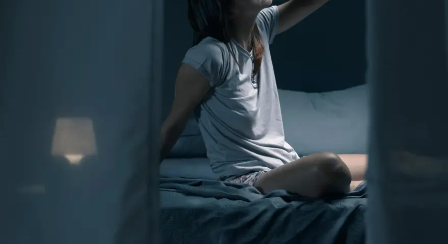 Frau sitzt im Bett, die Stirn gerunzelt, die Hand an der Stirn. Sie fragt sich, wie viel schwitzt man in der Nacht.