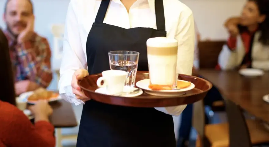 Kelnerka niesie tacę z kawą i wodą. Zastanawiasz się, ile zarabia barman w Sopocie?