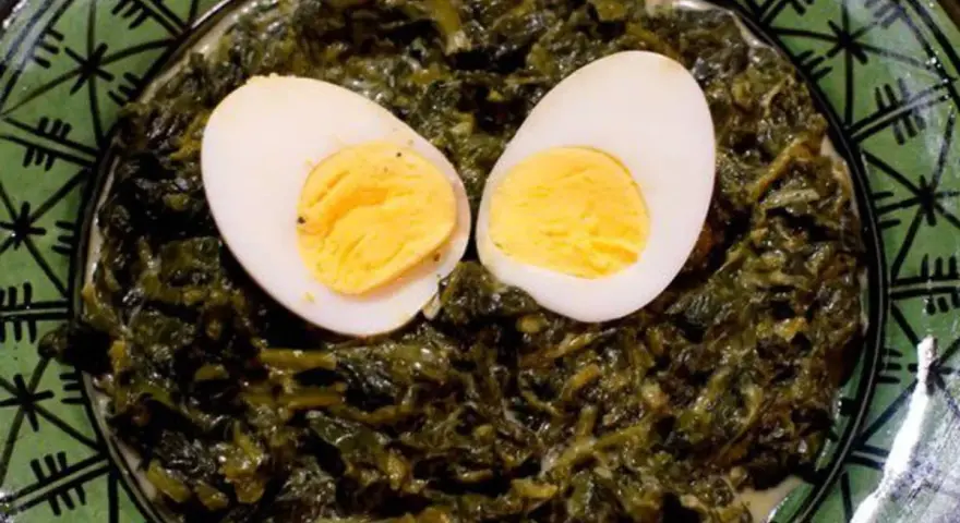 Un plat d'épinards à la crème, parsemé de deux moitiés d'œufs durs, sur une assiette verte décorée.