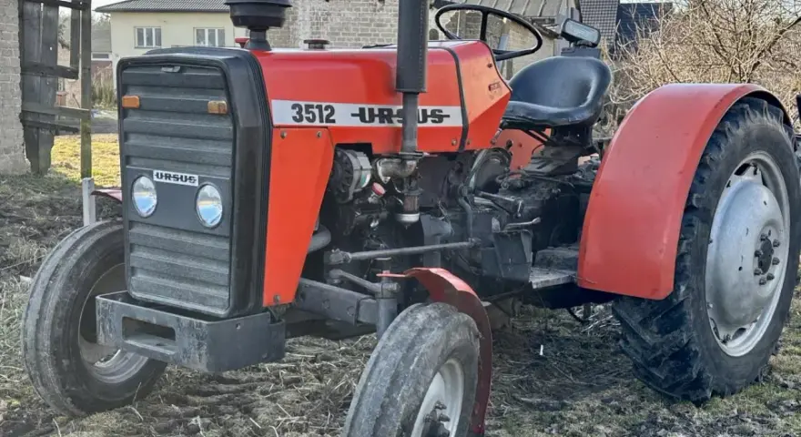 Czerwony ciągnik Ursus 3512 z czarną maskownicą i siedzeniem, stojący na ziemi.