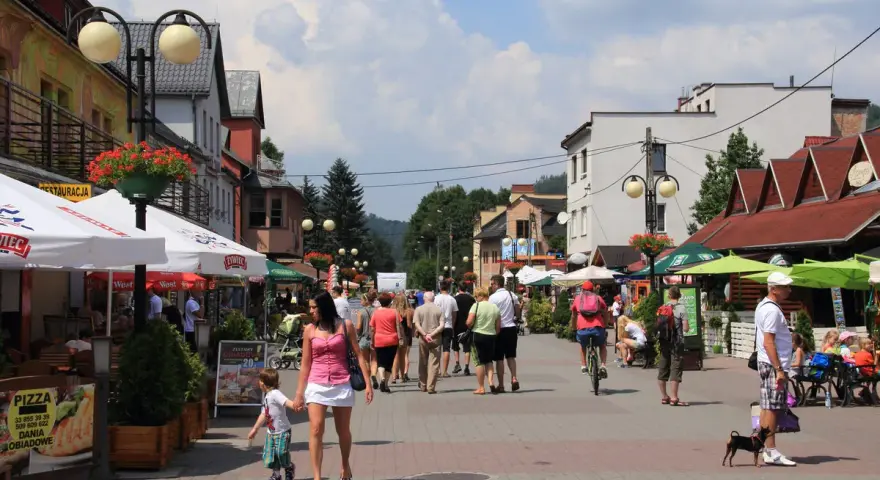 Tętniąca życiem ulica w Wiśle, pełna ludzi spacerujących, rowerzystów i psów. Wiele kawiarni i restauracji oferuje swoje atrakcje.