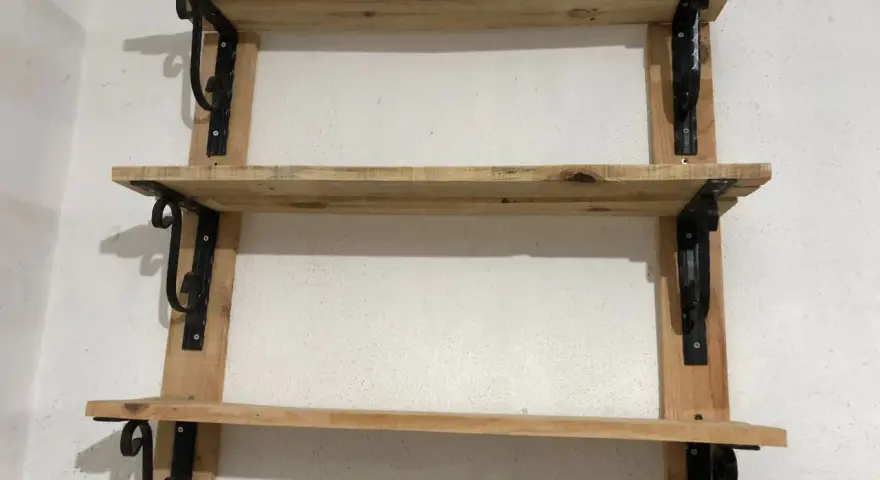 Scaffali fai da te garage: tre ripiani in legno grezzo, fissati a parete con staffe nere decorative. Perfetti per organizzare attrezzi e materiali.