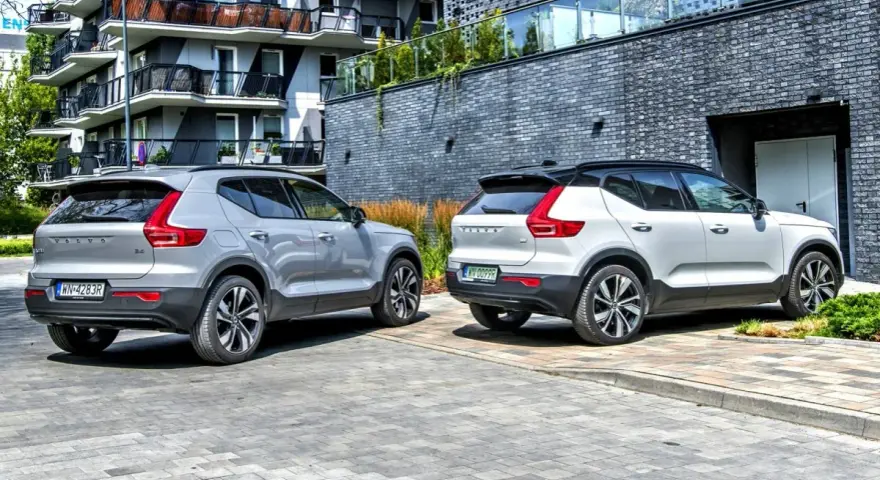Dwa modele Volvo XC40, jeden srebrny, drugi biały, zaparkowane przed nowoczesnym budynkiem.