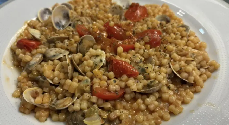 Un piatto invitante di fregola con vongole, pomodorini e prezzemolo, pronto per essere gustato.