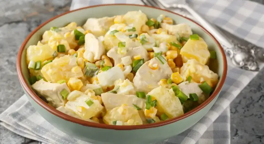 Una ciotola piena di insalata di pollo e patate, con mais, uova sode e cipollotto fresco.