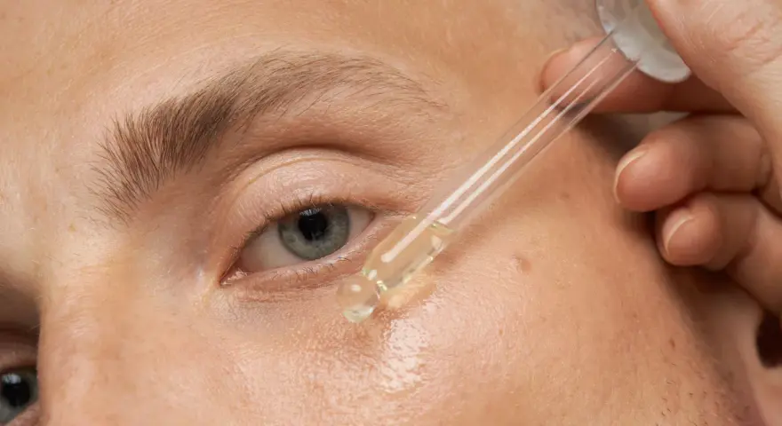 Nahaufnahme eines Auges, auf das ein Tropfen Öl aus einer Pipette aufgetragen wird.