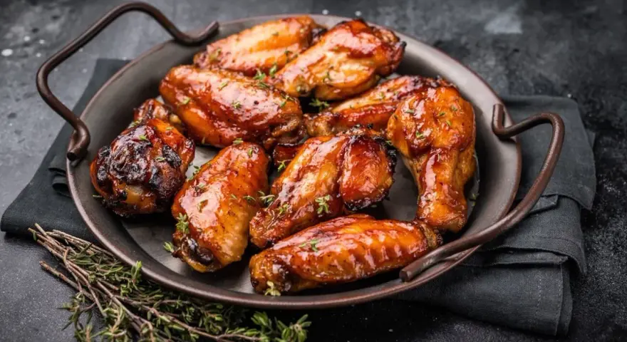 Saftige Hähnchenflügel in einer glänzenden Marinade, garniert mit frischem Thymian, serviert auf einer dunklen Platte.