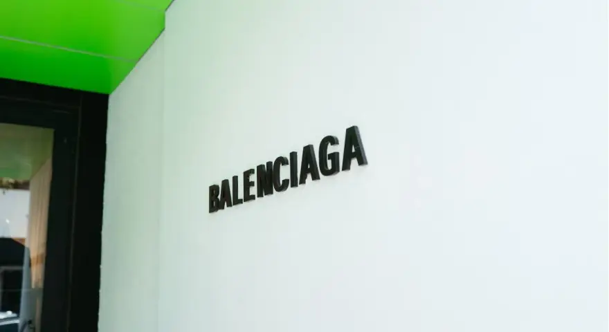 Il logo Balenciaga su una parete bianca, sotto un soffitto verde brillante. Chi è Balenciaga? Un nome che evoca alta moda e design audace.