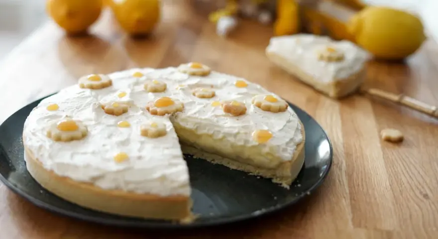 Tarte au citron décorée de petites fleurs en biscuit. Une part est coupée, révélant la crème pâtissière. Parfait pour une recette de tarte.