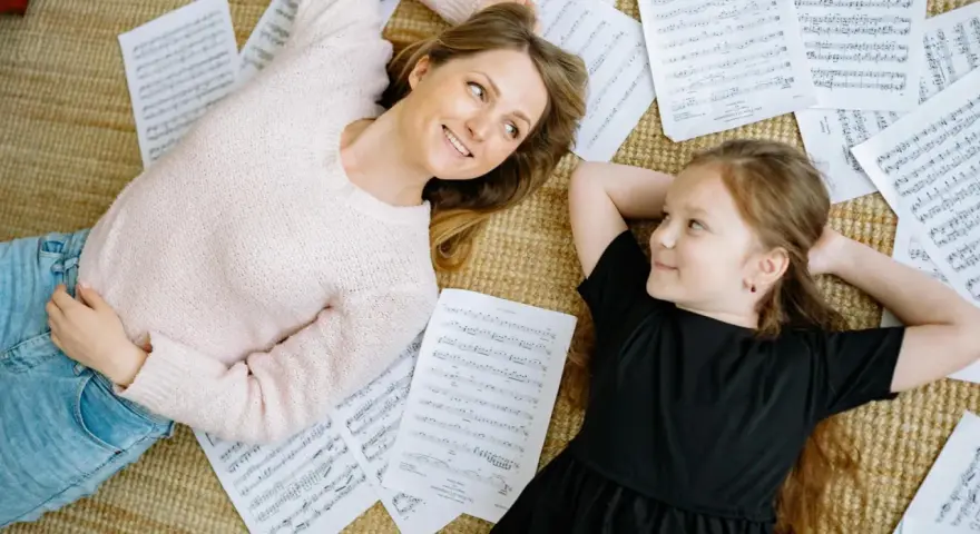 Mutter und Tochter liegen auf Notenblättern und lächeln sich an. Ein friedlicher Moment, der zeigt, wie Musik im Alltag verbindet.