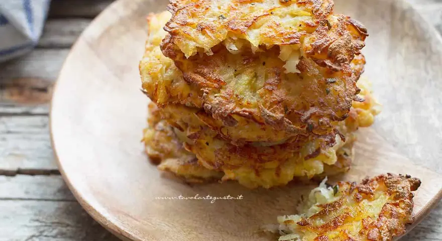 Una pila di dorate frittelle di patate, croccanti fuori e morbide dentro, servite su un piatto di legno.