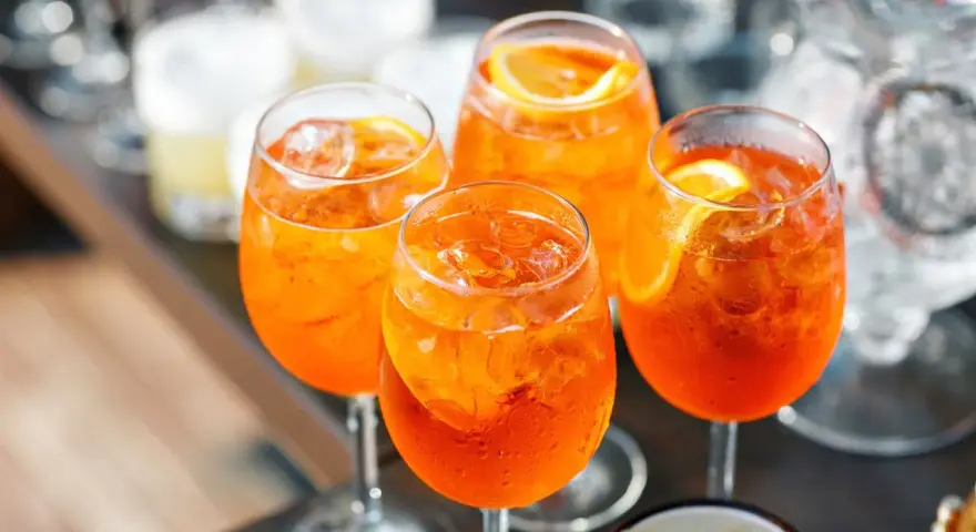Cztery orzeźwiające drinki Aperol Spritz z lodem i plasterkami pomarańczy. Idealny aperol przepis na letnie popołudnie.